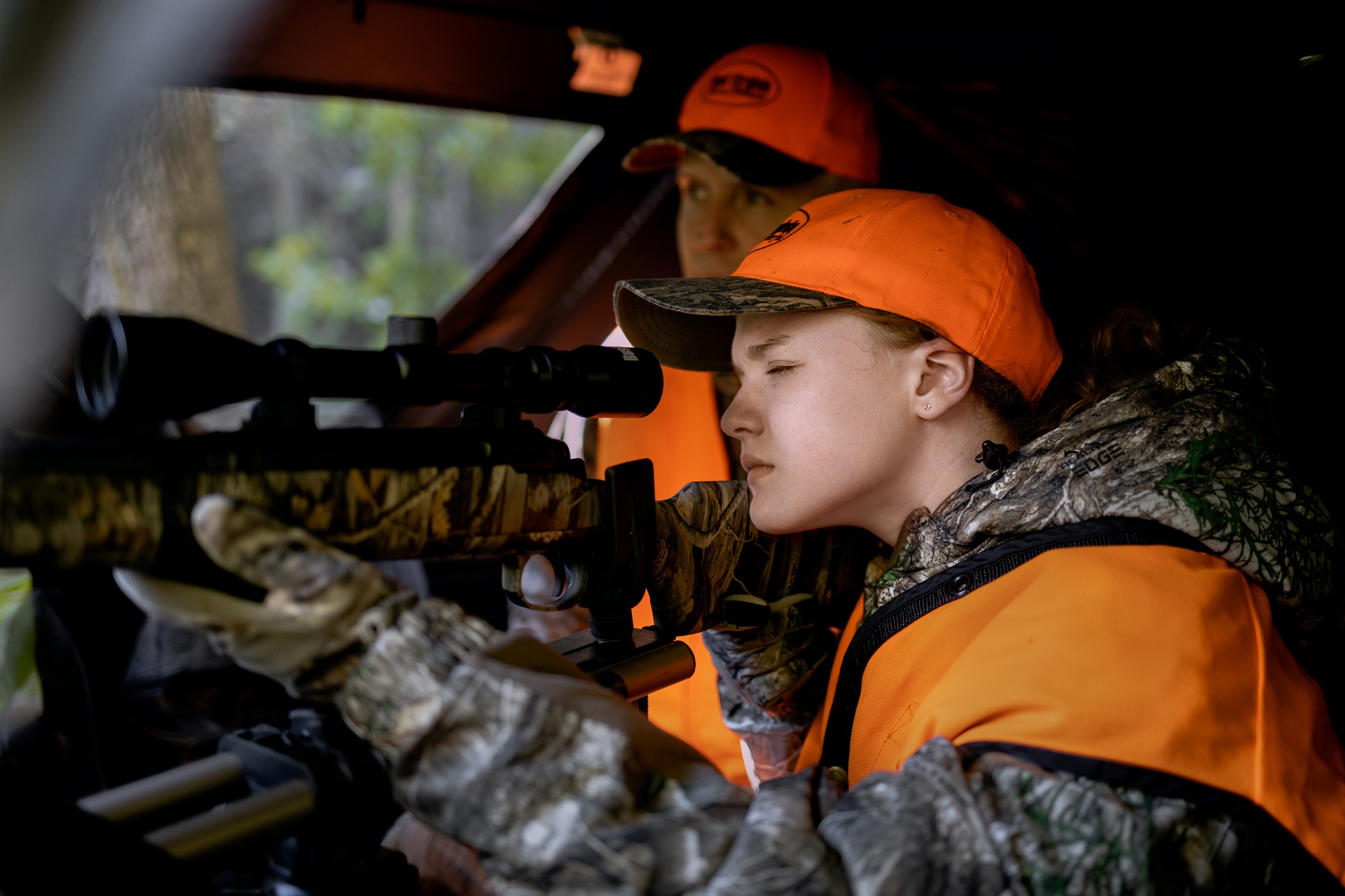 A father looks on as his son take aim from a hunting blind