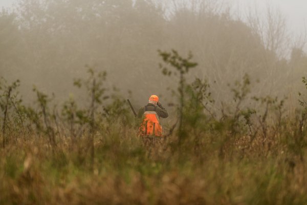 A lone hunter walks through a misty field.